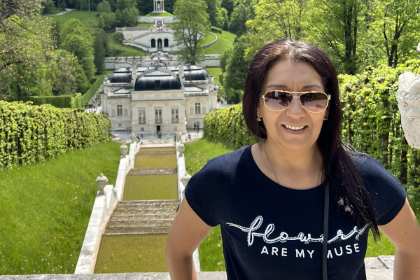 Frau mit Sonnenbrille vor einer historischen Garten- und Schlossanlage mit Treppen und Wasserachsen