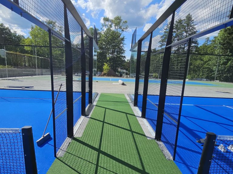Offener Zugang zu einem Padelplatz mit blauem Spielbelag und grünem Kunstrasen im Eingangsbereich