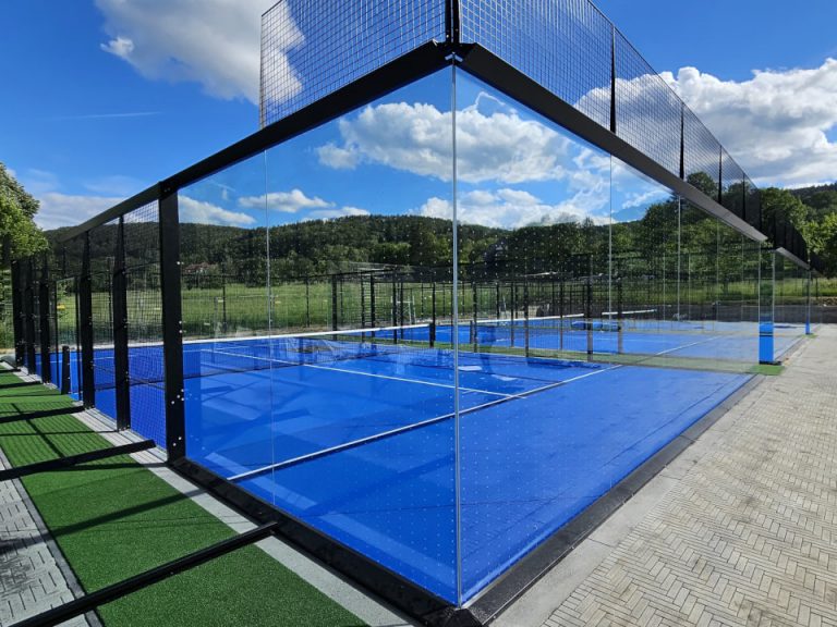 Padelplatz mit Glaswänden, schwarzer Stahlkonstruktion und blauem Spielbelag im Außenbereich