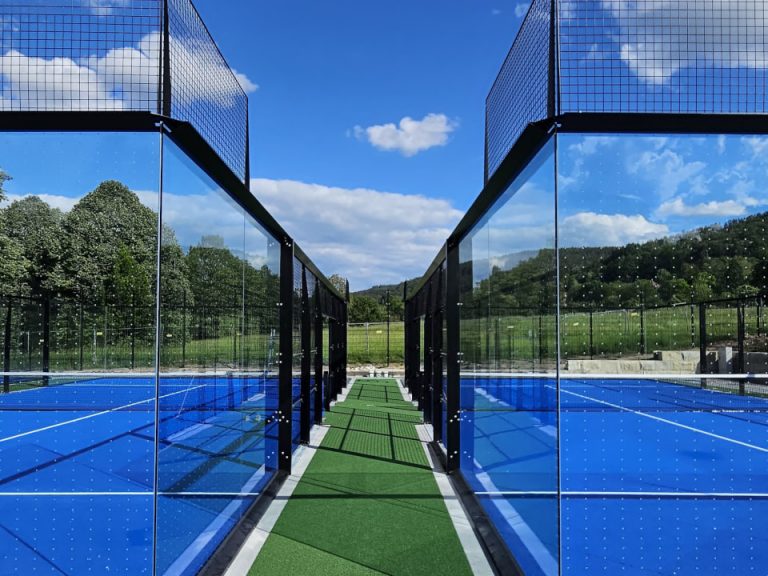 Zwischenweg zwischen zwei Padelplätzen mit Glaswänden, schwarzer Konstruktion und blauem Spielbelag