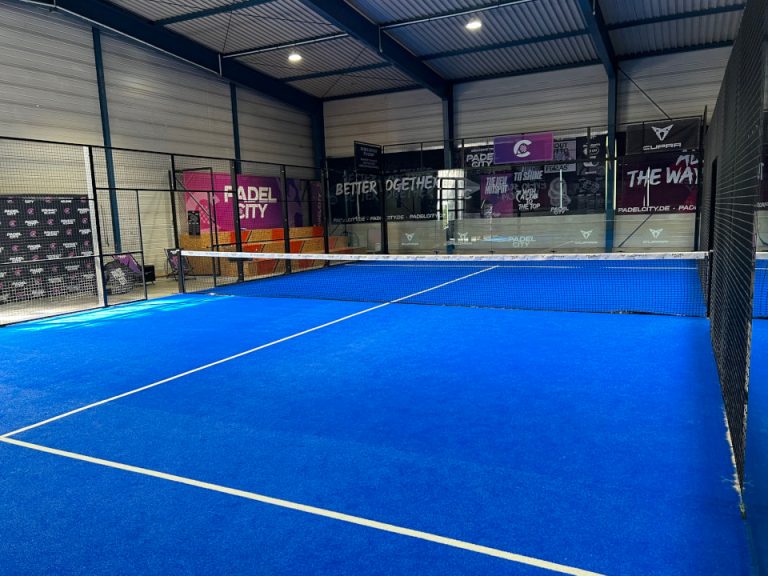 Indoor-Padelplatz mit blauem Spielbelag, Netz und transparenter Spielfeldabgrenzung