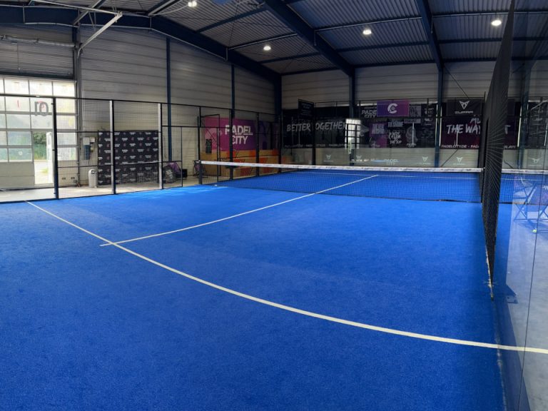 Indoor-Padelplatz mit blauem Spielbelag, Glaswänden und umlaufender Hallenkonstruktion