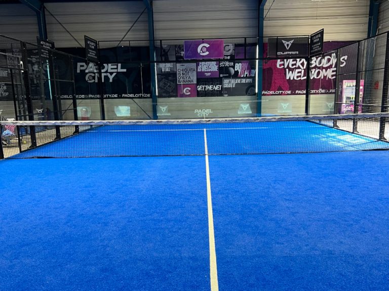 Indoor-Padelplatz mit blauem Spielbelag, Netz und markantem Club-Branding im Hintergrund