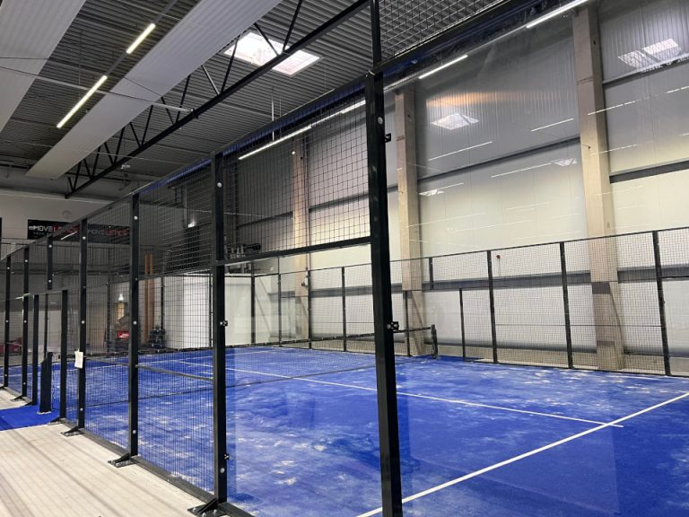 Indoor-Padelplatz mit Glaswänden, schwarzer Stahlkonstruktion und blauem Spielbelag