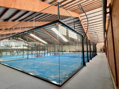 Seitliche Ansicht von Indoor-Padelplätzen mit Glaswänden in der Soccarena Heidelberg, Spieler auf dem Court, Holzwand rechts.